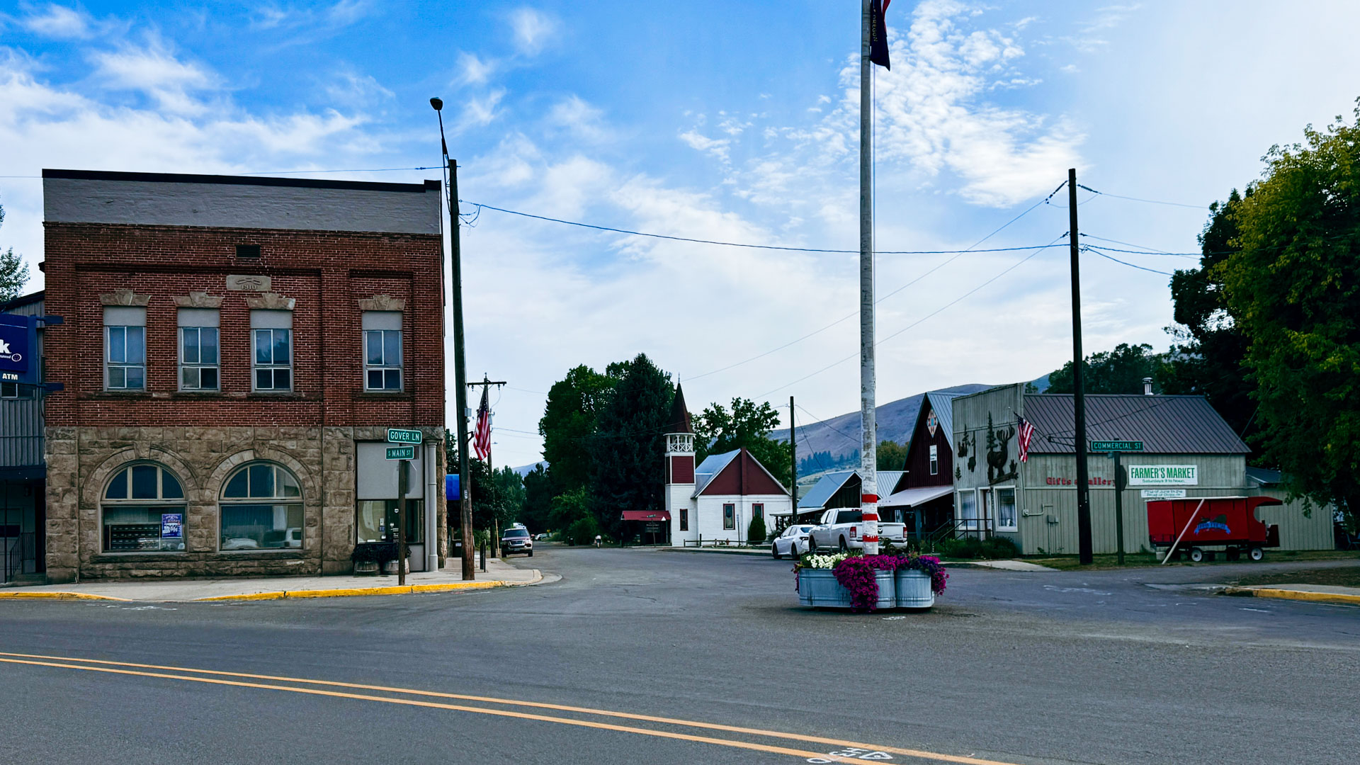 Halfway OR 5 A two-story brick building with an "US Bank" sign stands at a small town intersection with American flags and a flower planter in the foreground.