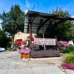 Halfway OR 15 A rustic outdoor venue in Halfway OR with a metal roof and hanging flower baskets displays a sign advertising Cowboy Breakfast: Famous Huckleberry Pancakes, Ham-Eggs & Local Fresh Melons. Trees and a horse-drawn wagon are in the background.